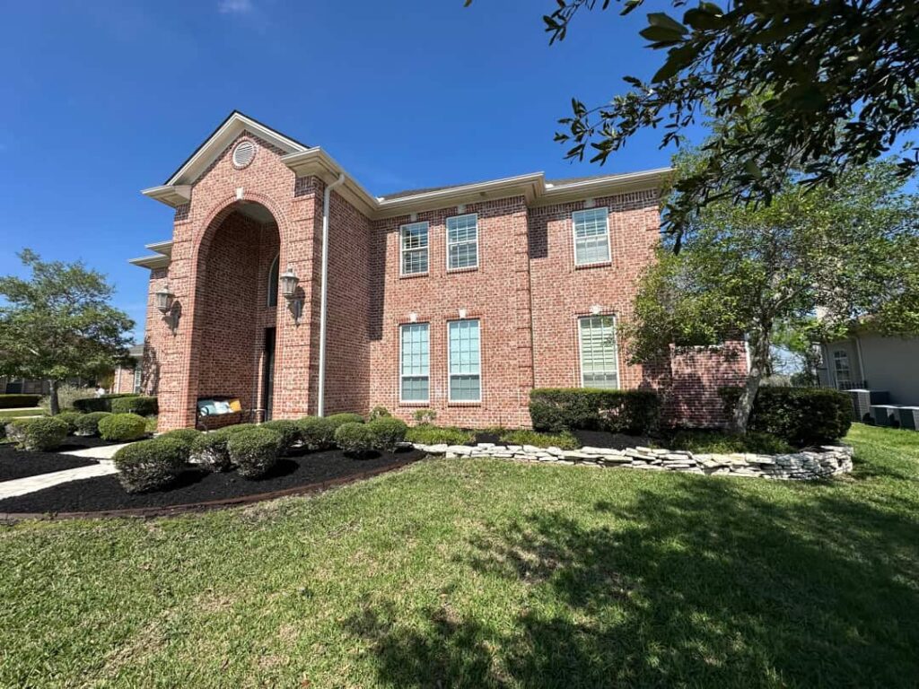 Two-story brick home in Bryan, TX with freshly mown lawn, trimmed shrubs and clean dark mulch beds